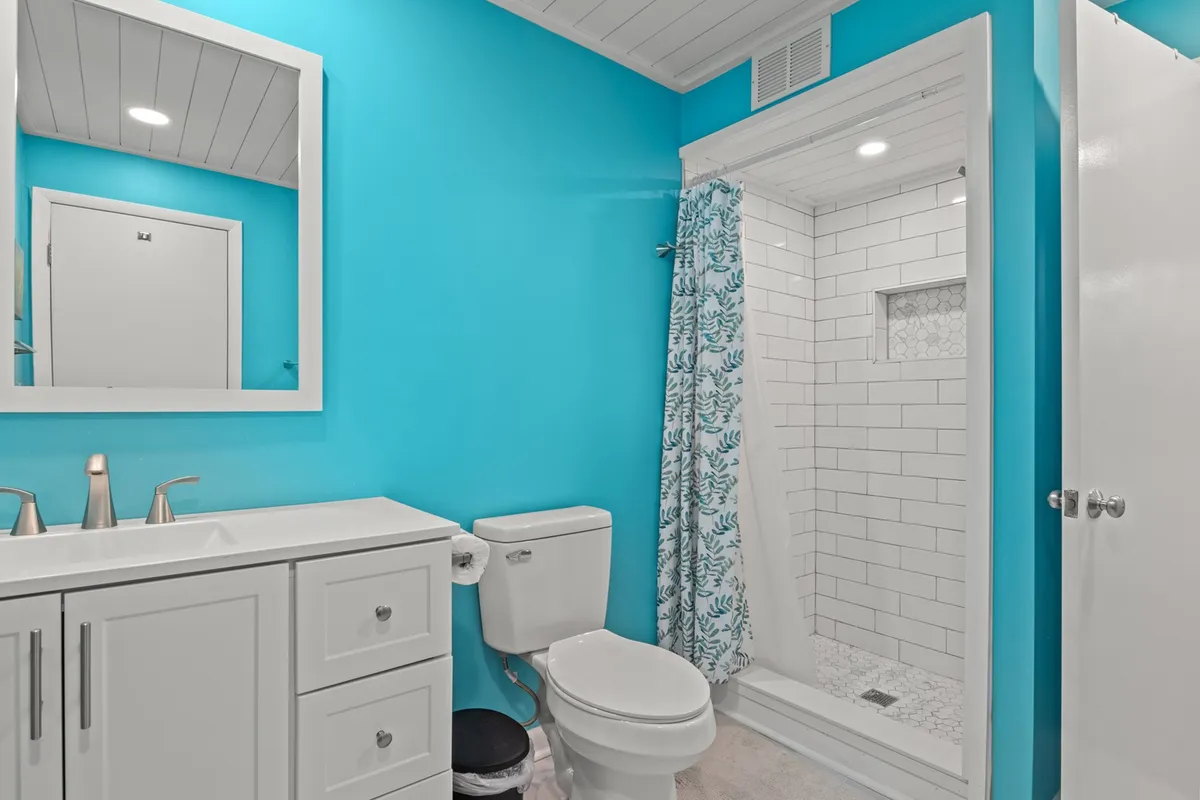 A vibrant bathroom featuring bright turquoise walls, a modern vanity, decorative shower curtain, and a large mirror. The space feels cheerful, energizing, and thoughtfully designed for daily routines.