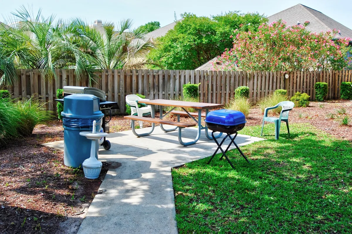 A casual, welcoming grilling area featuring a picnic table, a grill, manicured lawn, and landscaping. The scene is set for outdoor dining and socializing, with space for sunset barbecues and friendly gatherings.