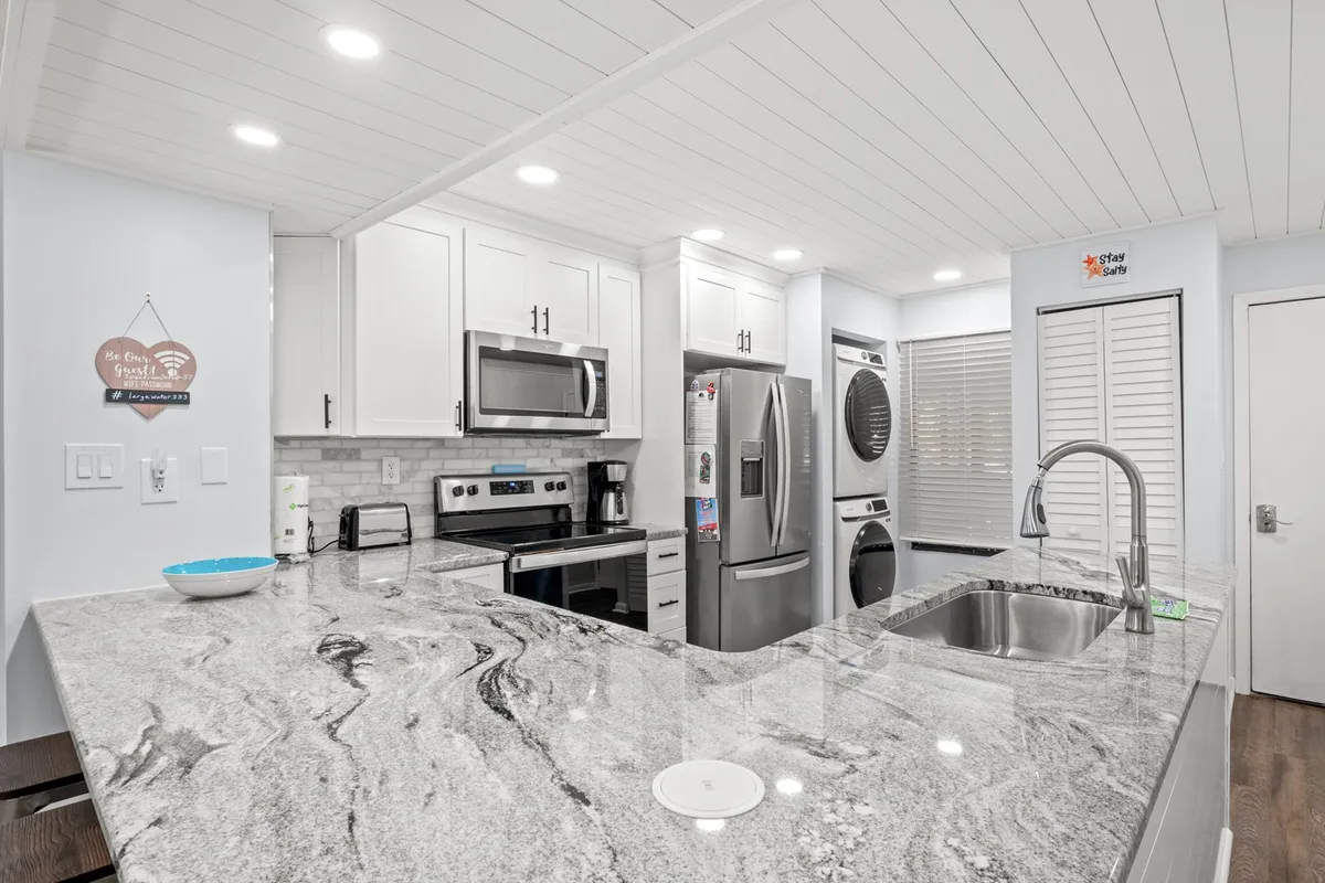 A spacious, welcoming kitchen featuring a gleaming granite countertop, stainless steel appliances, and crisp white cabinetry. The open layout hints at easy movement and social connection with adjacent living spaces, while modern fixtures invite culinary creativity.