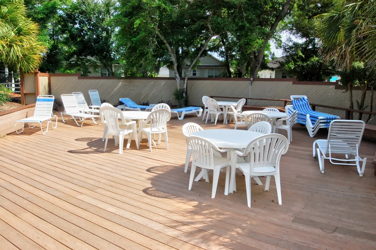 A tranquil yet social poolside area with tables and lounge chairs surrounded by trees, ideal for sunbathing, relaxed socializing, or outdoor dining. The scene evokes the spirit of sunset gatherings and pool parties, providing a welcoming environment for groups to connect.