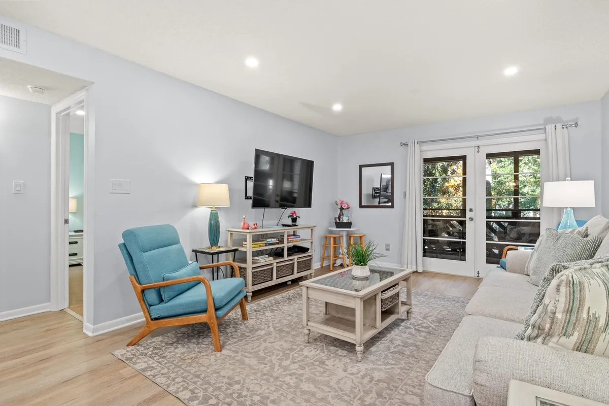 This image showcases a sunlit living room with a comfortable sofa, coffee table, TV, and armchair, along with a sliding door that invites natural light and possibly fresh coastal breezes. The arrangement is ideal for relaxing, watching movies, or socializing.