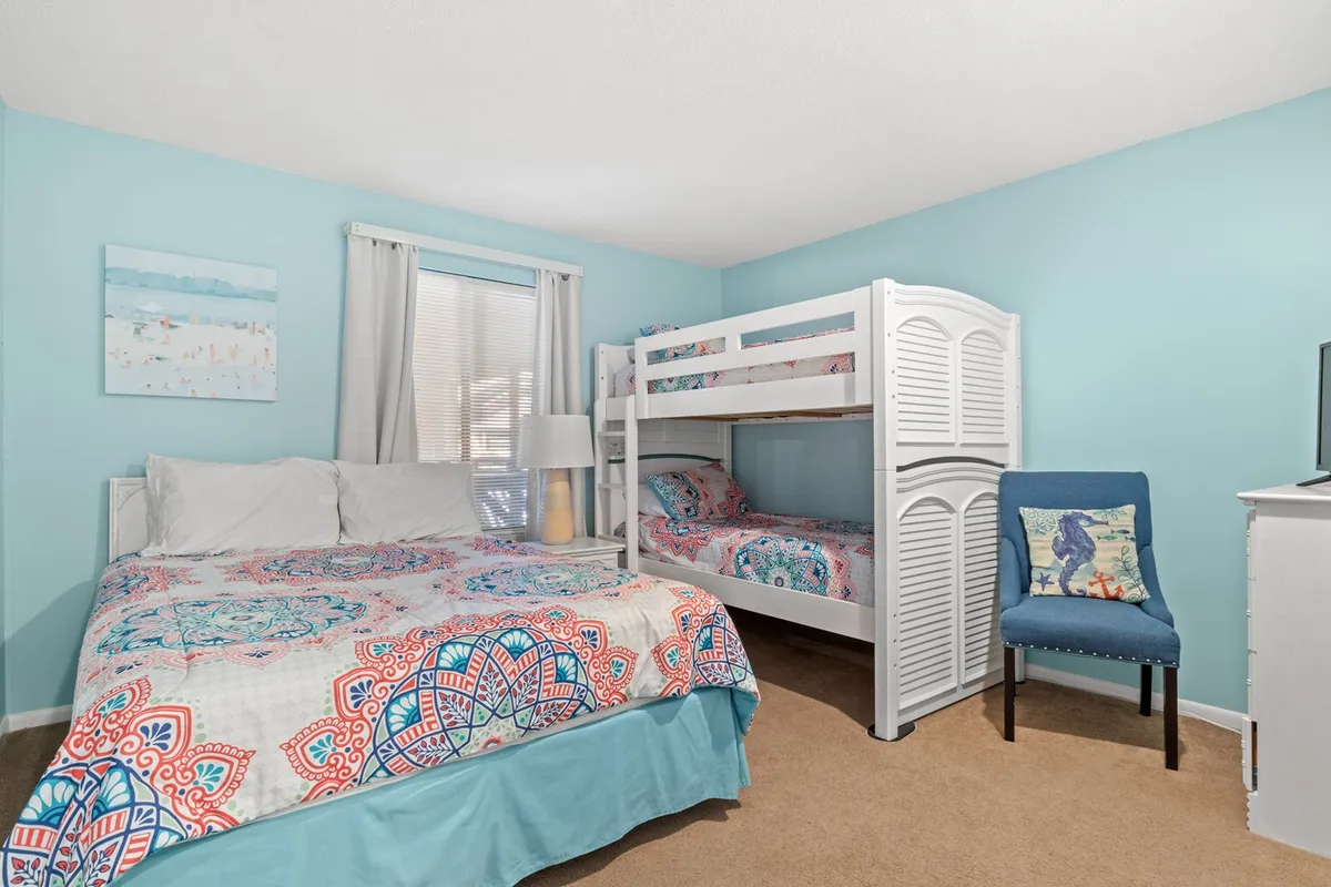 A cheerful bedroom with a queen bed, a bunk bed with colorful bedding, playful wall art, and a lamp. The mix of sleeping options makes the room ideal for families or groups, and the décor adds a relaxed, playful touch.