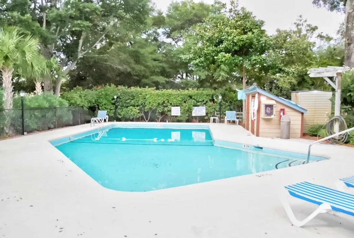 A sparkling outdoor swimming pool surrounded by poolside chairs, lush greenery, and a small shed. The area is tranquil and inviting, ideal for both relaxing swims and social gatherings. The atmosphere hints at leisurely afternoons spent sunbathing or enjoying a quiet book by the water.