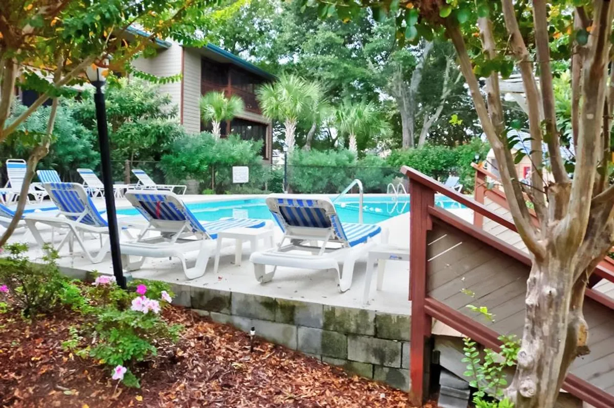 A sparkling swimming pool surrounded by lounge chairs and lush greenery, creating a tranquil and inviting environment for relaxation after a day of beachside adventures. The pool area appears spacious and family-friendly.