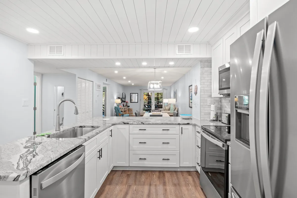 A bright, open kitchen with granite countertops, stainless steel appliances, white cabinetry, and an airy layout that blends seamlessly into adjacent entertaining spaces. The scene suggests a lively setting ideal for cooking and hosting.