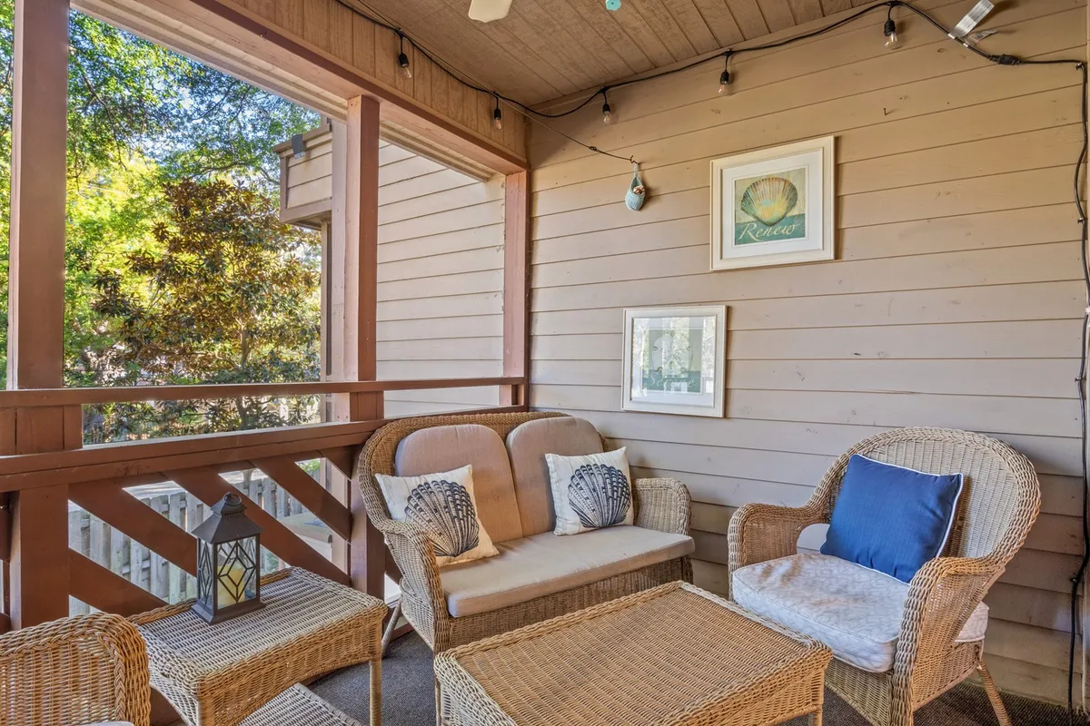 A cozy, screened porch furnished with wicker seating, a decorative lantern, and wall art. The porch offers a serene spot for relaxing, reading, or sipping drinks while enjoying views of nature in a comfortable setting.